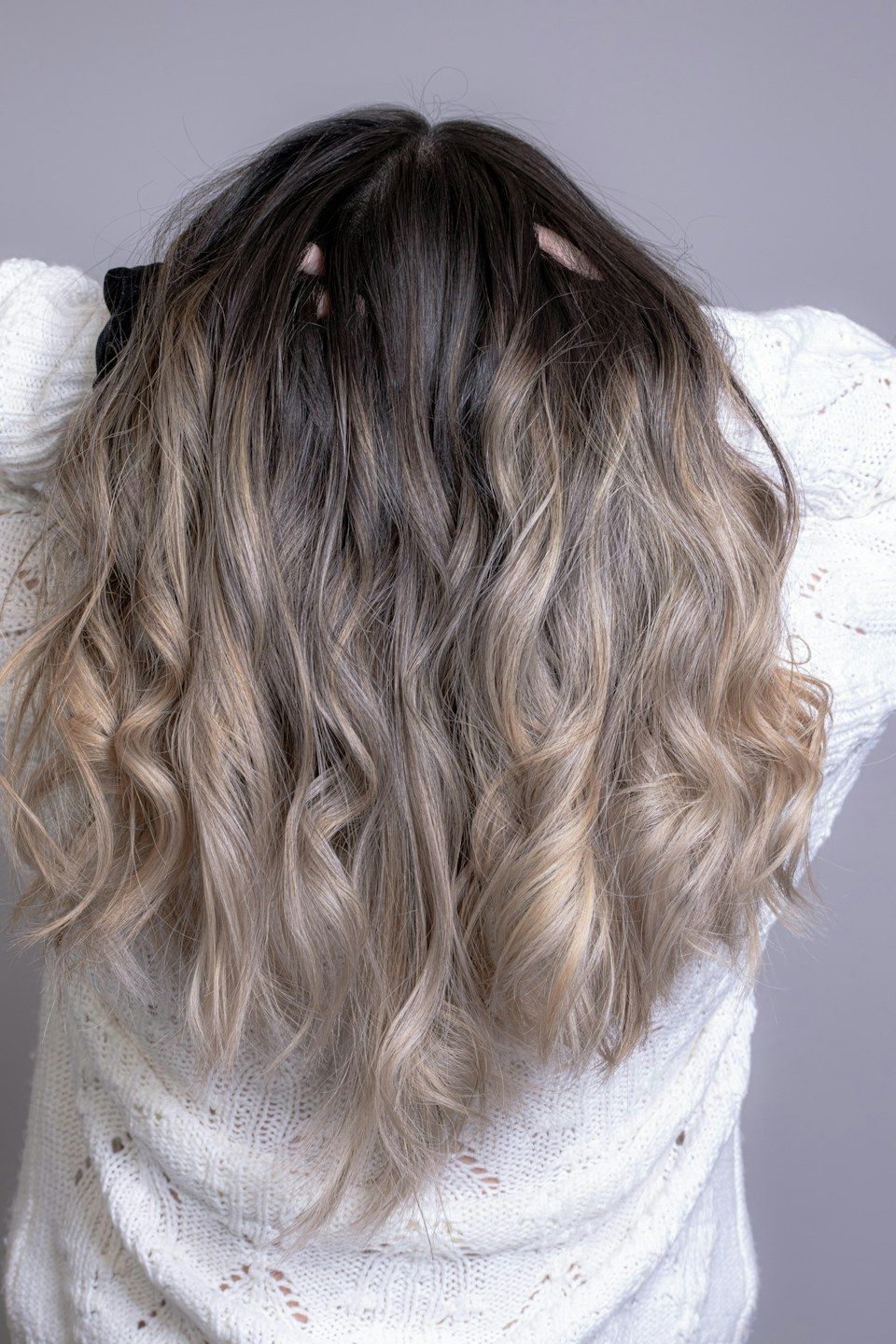 Cabelo ondulado com raiz escura e comprimento loiro acinzentado, visto de costas